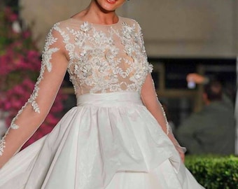 May include: A woman wearing a white wedding dress with a lace bodice and a flowing skirt. The dress has a fitted bodice with a sweetheart neckline and a full skirt that falls to the floor. The lace bodice is adorned with delicate floral appliques. The woman is smiling and looking at the camera.