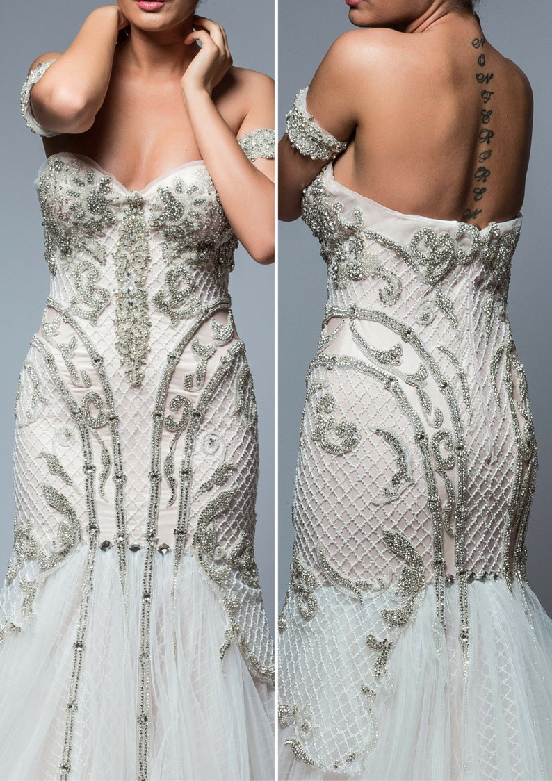 Puede incluir: Un vestido de novia blanco con un corpi&ntilde;o ajustado y una falda fluida. El corpi&ntilde;o est&aacute; cubierto de abalorios y bordados intrincados. La falda est&aacute; hecha de capas de tul y tiene una cola.