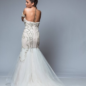 Puede incluir: Una mujer con un vestido de novia blanco con un corpi&ntilde;o de cuentas y una larga cola. El vestido tiene una silueta ajustada y un escote de coraz&oacute;n. La mujer est&aacute; de pie de espaldas a la c&aacute;mara, y su cabello est&aacute; recogido en un mo&ntilde;o.