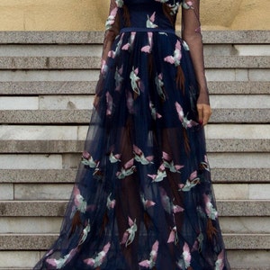 May include: A long, navy blue tulle dress with a sheer bodice and long sleeves. The dress is adorned with embroidered pink and green birds.