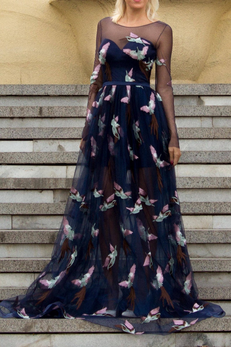 May include: A long, navy blue tulle dress with a sheer bodice and long sleeves. The dress is adorned with embroidered pink and green birds.