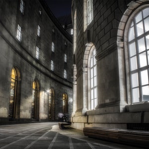 Puede incluir: Una fotografía en blanco y negro de un edificio con grandes ventanas arqueadas. El edificio tiene una fachada curva y está hecho de piedra. Las ventanas están todas abiertas y la luz del interior brilla hacia afuera.