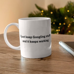 Könnte beinhalten: Weiße Keramik-Kaffeetasse mit schwarzer Aufschrift "Ich google einfach weiter und es funktioniert immer".