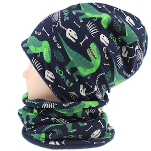 Peut inclure: Un ensemble de bonnet et cache-cou en tricot bleu et vert sur le thème des dinosaures. Le bonnet et le cache-cou présentent un motif répété de dinosaures verts, d'os et du mot "Roar!"