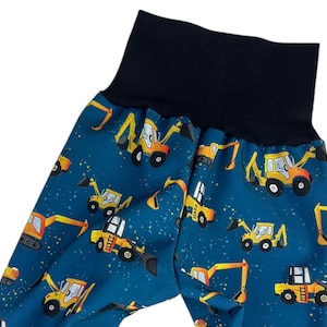 Può includere: Pantaloni blu con cintura nera e un motivo ripetuto di veicoli da costruzione gialli su uno sfondo blu con macchie bianche.