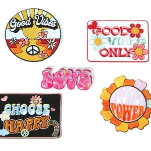 Könnte beinhalten: Eine Sammlung von gestickten Aufnähern mit einem Retro-Hippie-Thema. Designs umfassen einen runden Aufnäher mit "Good Vibes", einen rechteckigen Aufnäher mit "Good Vibes Only", einen Aufnäher mit dem Wort "Love", einen Aufnäher mit "Choose Happy" und einen Blumenaufnäher mit "Flower Power".