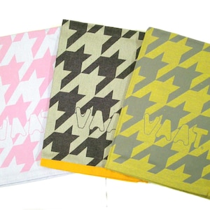 Może przedstawiać: Trzy złożone przedmioty z tkaniny z wzorem pepitki w kolorze różowym i białym, czarnym i beżowym oraz żółtym i szarym. Słowo "VAAT" jest wydrukowane na każdym przedmiocie w pasującym kolorze.