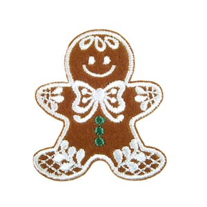 Könnte beinhalten: Ein brauner Lebkuchenmann-Aufnäher mit weißen Stickereidetails. Der Aufnäher hat ein lächelndes Gesicht, eine Fliege und grüne Akzente. Das Design erinnert an einen klassischen Weihnachtskeks.