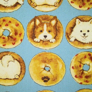 Könnte beinhalten: Ein blauer Hintergrund mit einem sich wiederholenden Muster aus gelben und braunen Bagels mit verschiedenen Hundeillustrationen. Die Hunde sind ein weißer Hund, ein brauner und weißer Hund und ein weißer Hund mit hoch erhobenem Schwanz.
