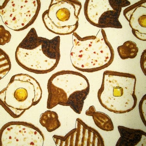 Könnte beinhalten: Ein weißer Stoff mit einem sich wiederholenden Muster aus braunen und gelben Toastformen. Einige der Toastformen haben ein Spiegelei, ein Katzen Gesicht oder ein Wirbelmuster.