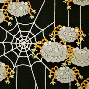 Könnte beinhalten: Ein schwarzer Stoff mit einem sich wiederholenden Muster aus Cartoon-Spinnen mit grauen Körpern, mehreren Augen und orange-gelb gestreiften Beinen, durchsetzt mit weißen Spinnennetz-Designs, die auf die Materialoberfläche gedruckt sind.