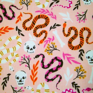 Op de afbeelding: Roze stof met een herhalend patroon van zwarte, witte, oranje en roze slangen, schedels en bloemmotieven.