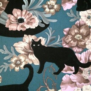 May include: A teal fabric with a black cat and a witch's hat. The fabric features a floral pattern with pink, brown, and white flowers.
