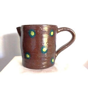 May include: A brown ceramic pitcher with a handle. The pitcher is decorated with green and yellow polka dots.