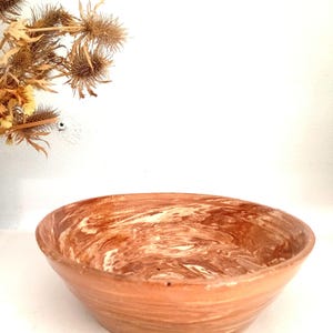 May include: A ceramic bowl featuring a marbled pattern of terracotta and cream colors. The bowl has a wide, circular opening and a smooth, rounded exterior surface. The interior displays swirling patterns of brown and white clay tones.