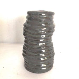 May include: A dark grey ceramic vase with a unique, wavy, textured design. The vase is tall and narrow, with a rounded base and a slightly flared opening.