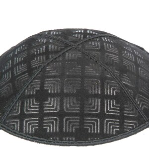 May include: Black kippah with a geometric pattern. The yarmulke features a textured design with a grid-like arrangement of squares and lines. The edges are neatly stitched, and the overall shape is rounded.