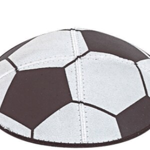 May include: A black and white soccer ball patterned kippah. The kippah is round with a black border and features the classic pentagon and hexagon design of a soccer ball. The stitching is visible, and the background is white.