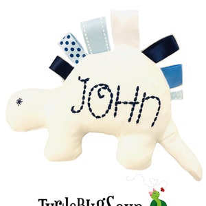 May include: White plush turtle toy with blue and white ribbons attached to its back. The turtle has the name "John" embroidered on its shell.