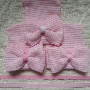May include: Three pink and white striped baby hats with bows. The hats are made of soft knit fabric and have a simple design. The bows are made of the same fabric as the hats and are tied in a simple knot.