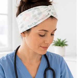 Pu&ograve; includere: Fascia bianca annodata, con un motivo di impronte di piedi di bambino rosa e grigio, e la parola "nurse". La persona indossa un camice blu e uno stetoscopio.