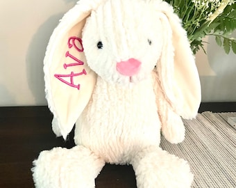 May include: A white plush bunny with long floppy ears. The bunny has a pink nose and black eyes. The bunny's ear is embroidered with the name "Ava" in pink thread.