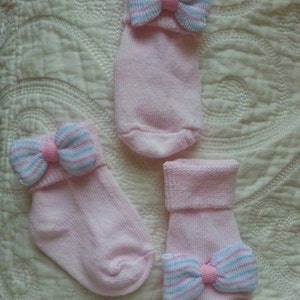 May include: Three pairs of pink baby socks with a blue and pink striped bow on each sock.