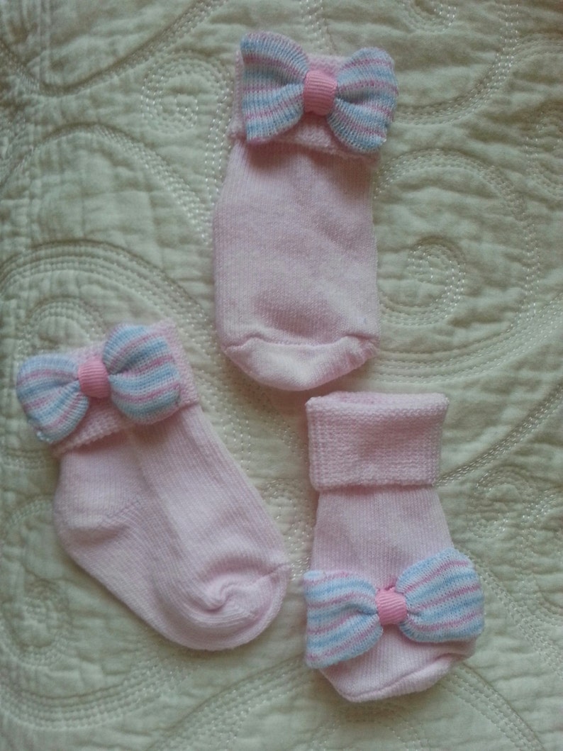 May include: Three pairs of pink baby socks with a blue and pink striped bow on each sock.
