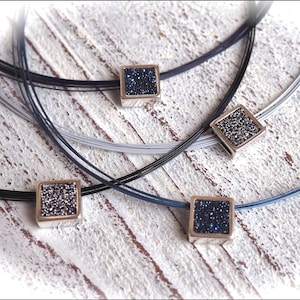 May include: Four layered necklaces with square pendants featuring a sparkly blue stone set in a silver frame.