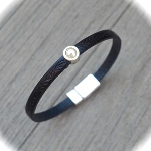 May include: A black leather bracelet with a silver magnetic clasp and a silver bead with a white pearl inlay.