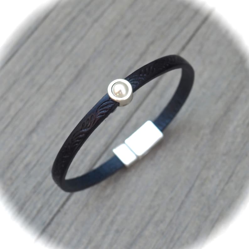 May include: A black leather bracelet with a silver magnetic clasp and a silver bead with a white pearl inlay.
