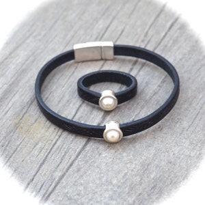 May include: A black leather bracelet and ring set with a pearl accent. The bracelet has a magnetic clasp and the ring is adjustable.