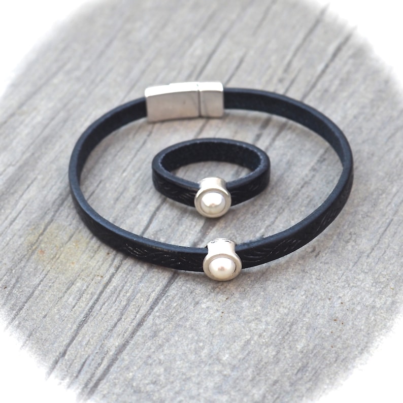 May include: A black leather bracelet and ring set with a pearl accent. The bracelet has a magnetic clasp and the ring is adjustable.