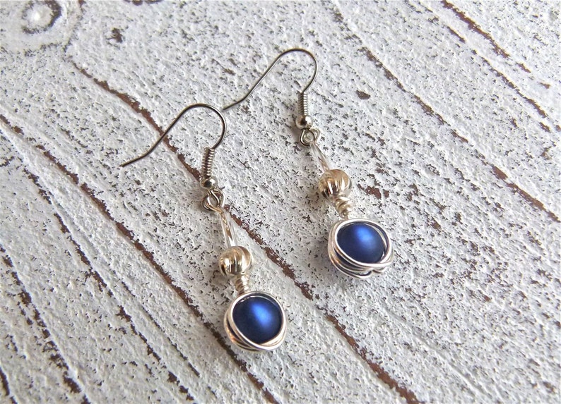 May include: A pair of silver dangle earrings with a blue iridescent bead and a silver bead on each earring.