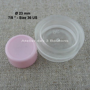 Peut inclure: Un bouton en plastique transparent de 23 mm de diamètre ou 7/8 pouces. Le bouton est marqué "Taille 36 US". Un bouton rose est également visible sur l'image.