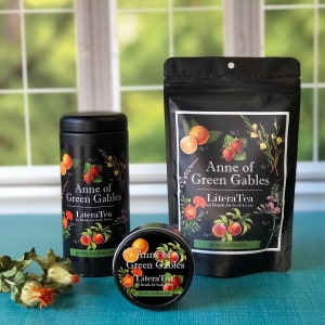 May include: Three black tea containers with labels featuring illustrations of oranges, strawberries, and flowers. The labels read "Anne of Green Gables Litera Tea two blends for book lovers" and "green rooibos tea".