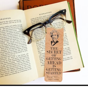 May include: A brown wooden bookmark with the text "The Secret of Getting Ahead is Getting Started" and the author's name "Mark Twain" in a smaller font. The bookmark features a vintage-style illustration of Mark Twain.