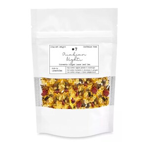 May include: A white pouch of loose leaf tea with a clear window displaying the tea blend. The label reads "#7 Arabian Nights Turmeric Ginger Loose Leaf Tea." The tea blend includes apple pieces, rosehips, turmeric, ginger, mango, and black peppercorn. The pouch is caffeine-free.