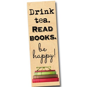 K&ouml;nnte beinhalten: Holz-Lesezeichen mit dem Text "Drink tea. READ BOOKS. be happy!" und einem Stapel B&uuml;cher und Brillen darauf.
