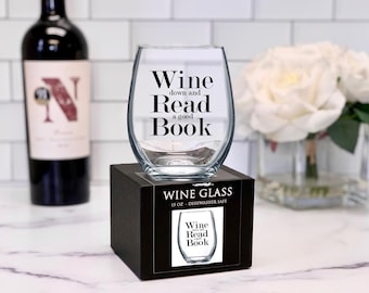 Könnte beinhalten: Ein klares Weinglas aus Glas mit dem aufgedruckten Text "Wine down and Read a good Book". Das Glas steht auf einer schwarzen Box mit dem gleichen aufgedruckten Text.