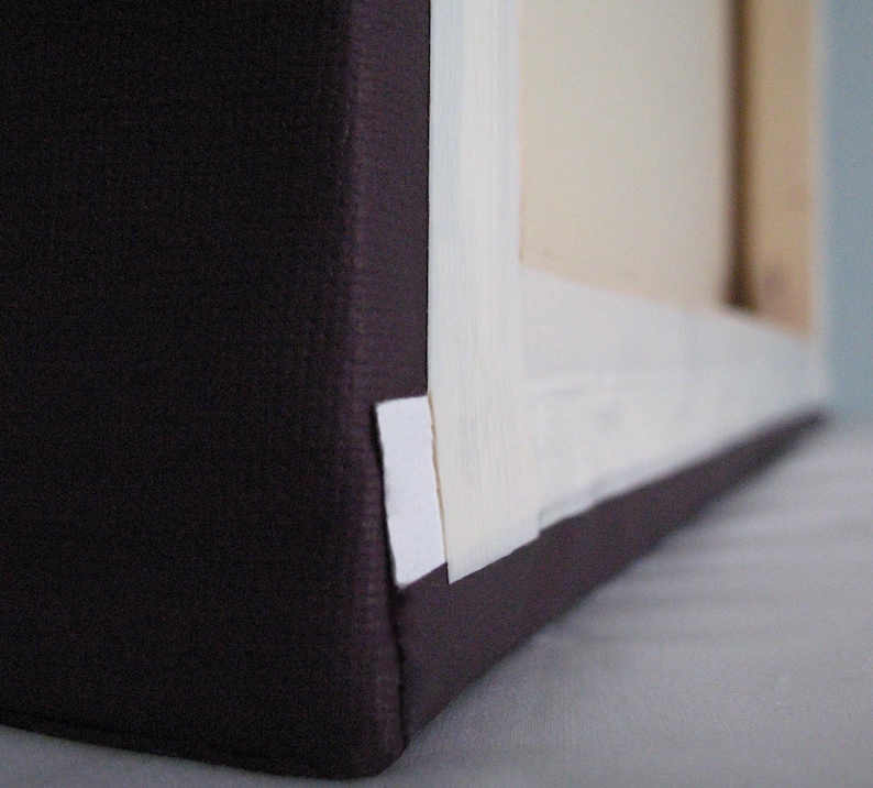 May include: Close-up of a wrapped canvas art piece. The canvas is stretched over a wooden frame and wrapped with a dark purple fabric. White tape secures the canvas to the frame.
