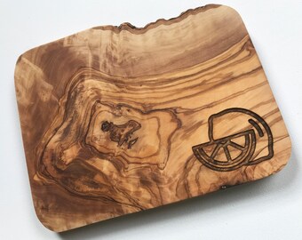 May include: A small, rectangular olive wood serving board with a natural wood grain pattern. The board has a carved lemon design on one end.