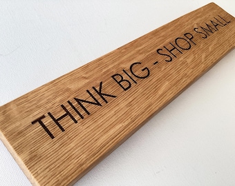 May include: A wooden sign with the text "Think Big - Shop Small" engraved in black lettering.