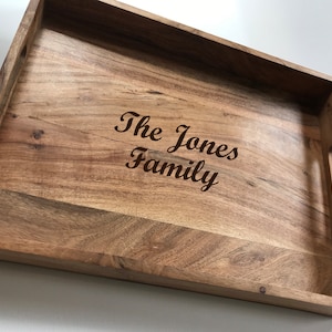 May include: A wooden serving tray with a natural wood finish and two handles. The tray is engraved with the text "The Jones Family".