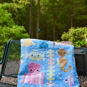 May include: A blue and white quilt with a seahorse, octopus, and fish design. The quilt is folded and sitting on a metal swing set.