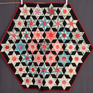 May include: A hexagonal quilt with a black and white geometric pattern and red and blue flower designs in the center of each hexagon.