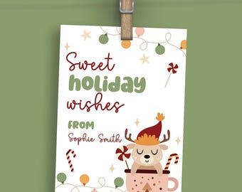 May include: A white gift tag with the text "Sweet holiday wishes from Sophie Smith" is clipped to a string. The tag features a reindeer in a mug with candy canes and festive lights.