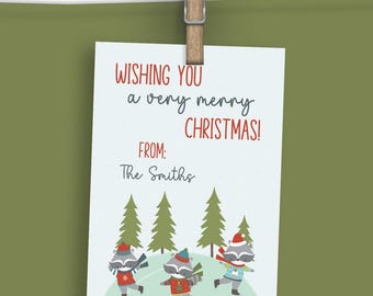 May include: A white Christmas card with the message "Wishing you a very merry CHRISTMAS!" in red and black text. The card features illustrations of raccoons in festive outfits and green Christmas trees. The card is clipped to a clothesline.