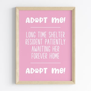 Può includere: Un cartello stampabile rosa con il testo "ADOPT me!" e "LONG TIME SHELTER RESIDENT PATIENTLY AWAITING HER FOREVER HOME" in testo bianco. Il cartello include anche una grafica di impronta di zampa. Il testo "ADOPT me!" appare due volte sul cartello. Il cartello è incorniciato in una cornice di legno chiaro.