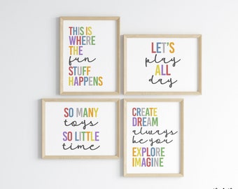 May include: Four framed prints with colorful text on a white wall. The prints feature phrases like "This is where the fun stuff happens", "Let's play all day", "So many toys, so little time", and "Create, dream, always be you, explore, imagine".
